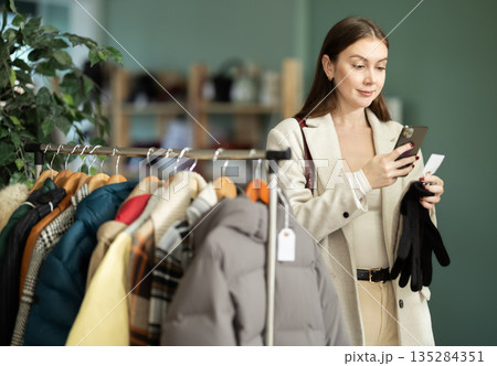 Young woman scanning QR-code on gloves in clothing store Young woman scanning QR-code on gloves in clothing store 135284351