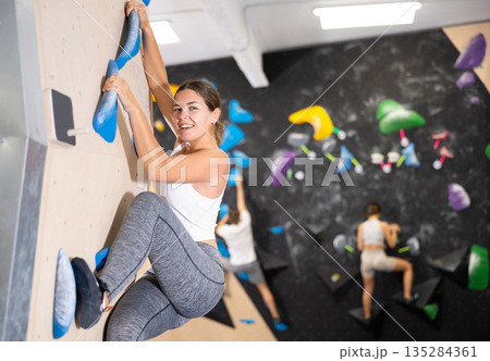 Cheerful girl climbing colored artificial wall without safety rope Cheerful girl climbing colored artificial wall without safety rope 135284361