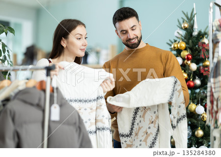 Couple choosing a warm sweater against the background of a Christmas tree in a decorated store 135284380