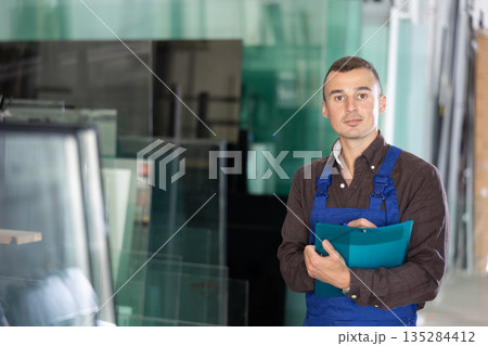 Positive factory worker with clipboard standing in glass workshop Positive factory worker with clipboard standing in glass workshop 135284412