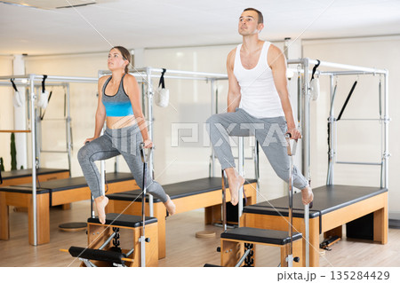Athletic girl and man doing stretching on pilates machine in pilates studio Athletic girl and man doing stretching on pilates machine in pilates studio 135284429