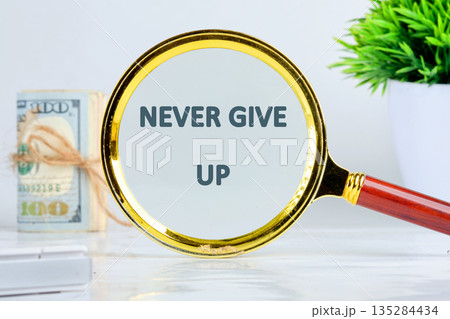 A golden magnifying glass highlights the words NEVER GIVE UP, with a stack of money tied with twine and a small plant in the background, suggesting financial success and resilience A golden magnifying glass highlights the words NEVER GIVE UP, with a stack of money tied with twine and a small plant in the background, suggesting financial success and resilience 135284434