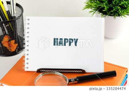 The concept shows a notebook with the word Happy written on it. Office supplies, a plant, books, and a magnifying glass decorate the bright white surface The concept shows a notebook with the word Happy written on it. Office supplies, a plant, books, and a magnifying glass decorate the bright white surface 135284474