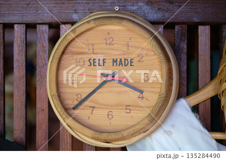 A circular, light wooden clock with black hands, a red second hand, and engraved numerals shows the current time. The words SELF MADE are prominently featured on the clock face 135284490