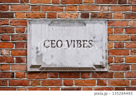 A stone plaque with the words CEO VIBES in capital letters is attached to a red brick wall. The bricks are a mix of shades and textures A stone plaque with the words CEO VIBES in capital letters is attached to a red brick wall. The bricks are a mix of shades and textures 135284493