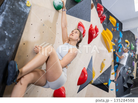 Young girl moving on bouldering wall at indoor climbing gym 135284508