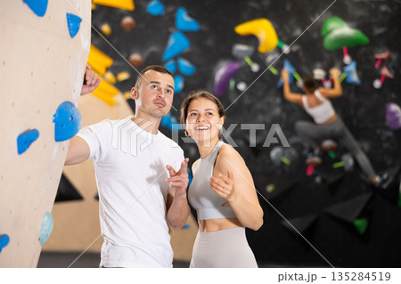 Girl gym coach and teen client standing in fitness room discussing possible options climbing 135284519
