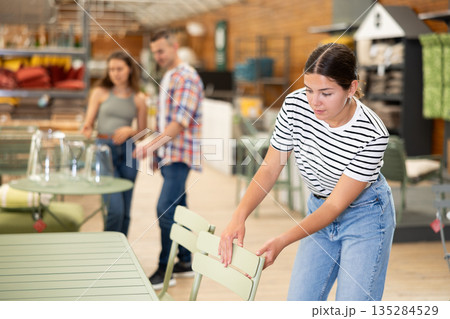 Girl thoughtfully choosing practical patio chairs in garden store Girl thoughtfully choosing practical patio chairs in garden store 135284529