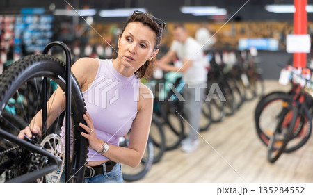 Female cyclist carefully examining bike wheel in store Female cyclist carefully examining bike wheel in store 135284552