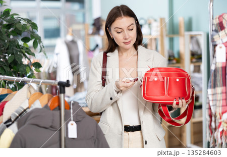 Happy woman choosing a fashionable handbag in boutique Happy woman choosing a fashionable handbag in boutique 135284603