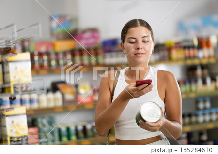 Female shopper scanning barcode or qr code with smartphone on canned food label Female shopper scanning barcode or qr code with smartphone on canned food label 135284610