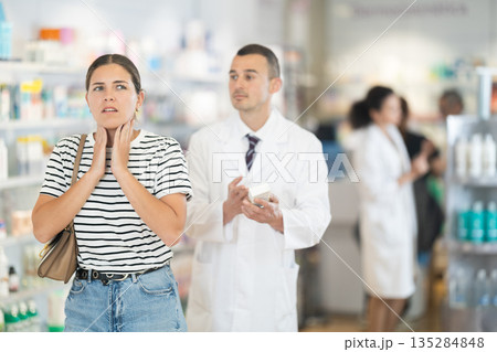Young girl feeling pain standing with her back to male pharmacist offering remedy Young girl feeling pain standing with her back to male pharmacist offering remedy 135284848