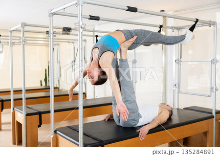 Couple practicing acroyoga on Pilates trapeze table in studio Couple practicing acroyoga on Pilates trapeze table in studio 135284891