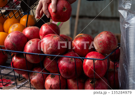 A woman with light skin and long nails picks a pomegranate from a black plate. The pomegranates are red and partially opened, revealing seeds. A woman with light skin and long nails picks a pomegranate from a black plate. The pomegranates are red and partially opened, revealing seeds. 135284979