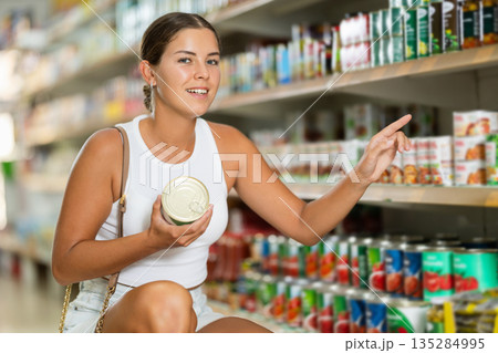 Girl is shopping in grocery department of supermarket - choosing canned goods 135284995
