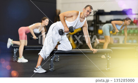Athletic man pumping her biceps with a dumbbell while leaning on bench Athletic man pumping her biceps with a dumbbell while leaning on bench 135285000