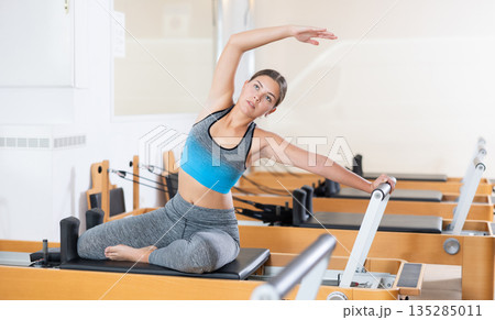 Girl doing stretching exercises on reformer in pilates studio 135285011
