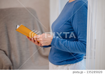 Woman in blue sweater holding orange notebook, anonymous education and planning concept Woman in blue sweater holding orange notebook, anonymous education and planning concept 135285020