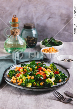 Vegetarian salad with chickpeas, tomatoes, broccoli and greens on a plate on the table vertical view 135285052
