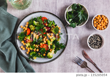 Vegetarian salad with chickpeas, tomatoes, broccoli and greens on a plate on the table top view 135285054