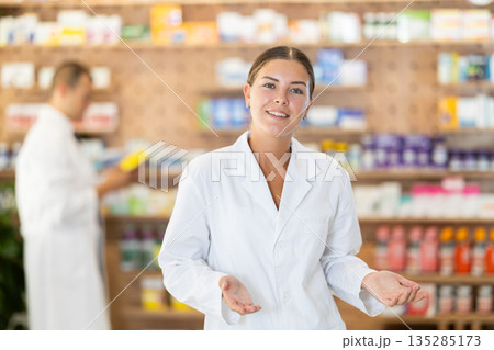 At pharmacy, girl apothecary waiting for customers, invite with gesture go to department of cosmetic 135285173