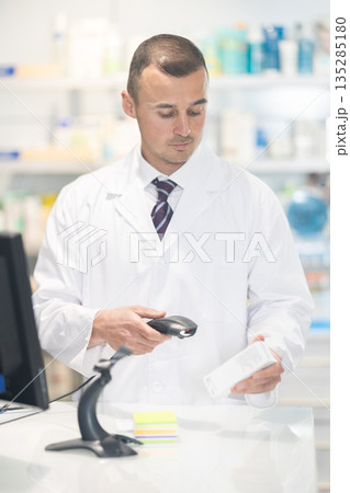 Young male pharmacist pushing medicine at cash register Young male pharmacist pushing medicine at cash register 135285180
