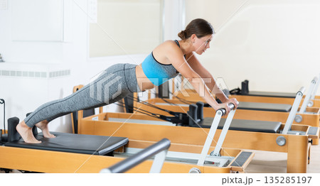 Young girl performing pilates exercises on reformer in studio 135285197