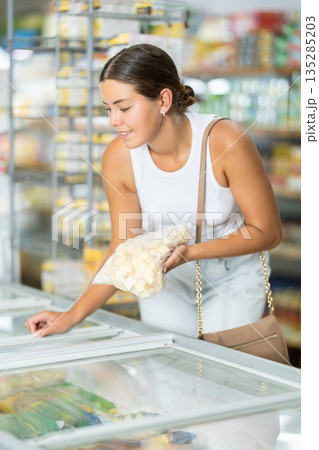 Girl supermarket visitor chooses frozen semi-finished products traditional Russian dumpling 135285203