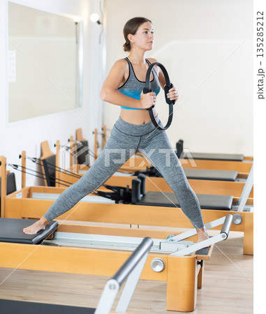 Fit girl doing exercises with resistance ring on Pilates reformer 135285212