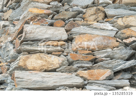 Close-up of stacked flat stones forming a natural wall texture. Rustic background for design and architecture concepts Close-up of stacked flat stones forming a natural wall texture. Rustic background for design and architecture concepts 135285319