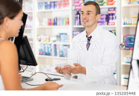 Male pharmacist consulting young girl about medicament in box Male pharmacist consulting young girl about medicament in box 135285448