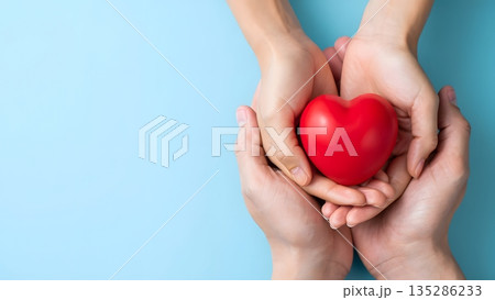 Hands Holding a Red Heart on a Blue Background Symbolizing Love 135286233