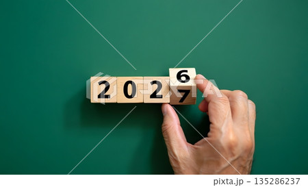 Hand Changing Year on Wooden Blocks from 2026 to 2027 on Green Background Hand Changing Year on Wooden Blocks from 2026 to 2027 on Green Background 135286237