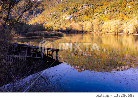 Autumn Lake Scene With Reflections, Mountains, And A Weathered Dock By Calm Water 135286688