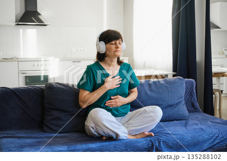 Woman closing eyes, listening to music, and focusing on breathing for relaxation 135288102