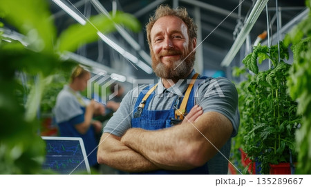 Confident startup founder in front of vertical farm with solar panels and digital sensors showcasing green innovation 135289667