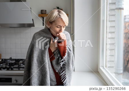 Middle aged woman in plaid showing signs of cold and flu, heavy coughing and sore throat symptoms. Middle aged woman in plaid showing signs of cold and flu, heavy coughing and sore throat symptoms. 135290266