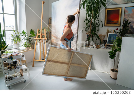 Creative woman artist enjoying art therapy hobby at home studio, placing paintings on easel. Creative woman artist enjoying art therapy hobby at home studio, placing paintings on easel. 135290268