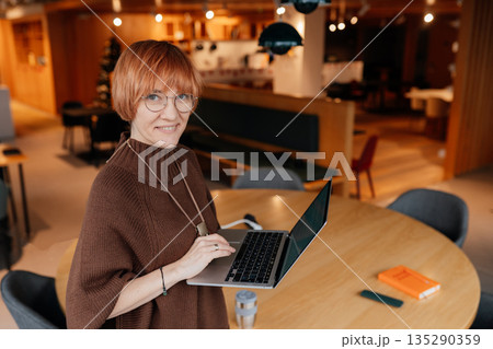 Adult professional woman using laptop at large table in contemporary coworking interior. Female entrepreneur during focused work, modern business lifestyle, office, workspace, technology, copy space Adult professional woman using laptop at large table in contemporary coworking interior. Female entrepreneur during focused work, modern business lifestyle, office, workspace, technology, copy space 135290359