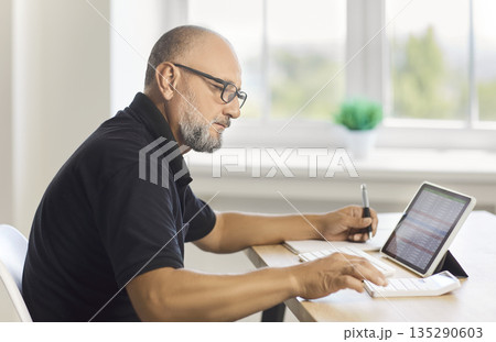Mature man working with spreadsheet on tablet and calculator at home office 135290603