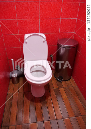 Toilet room with toilet bowl, wastebasket, toilet brush and red wall tiles 135292032