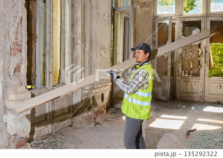 Focused worker in safety gear assesses measurement by sunlit arched window Focused worker in safety gear assesses measurement by sunlit arched window 135292322