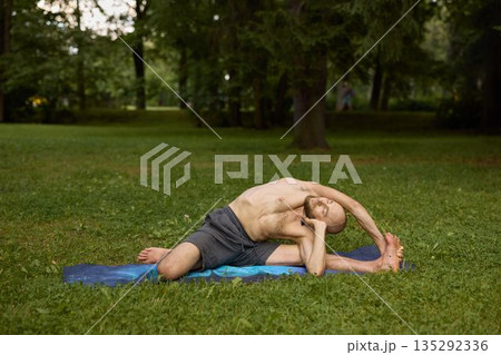 Individual executing deep side stretch on blue exercise mat outdoors Individual executing deep side stretch on blue exercise mat outdoors 135292336