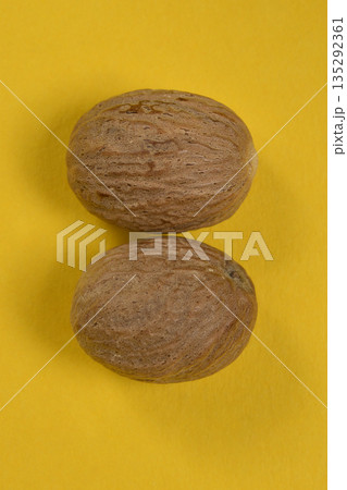 Two whole nutmeg seeds on yellow background Two whole nutmeg seeds on yellow background 135292361