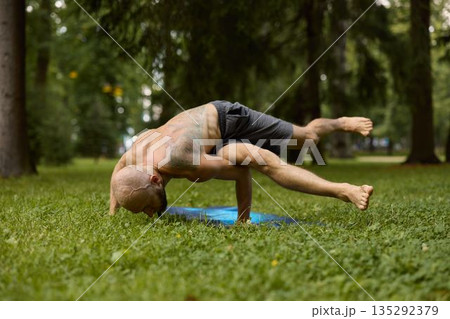 Athletic man controlling core stability amidst lush greenery 135292379