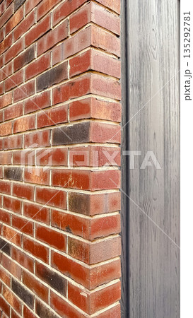 Close-up of a red brick wall corner adjacent to grey wooden siding with visible texture and grain 135292781