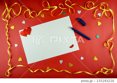 Blank white paper card with pen and red hearts on red background with gold ribbon border. 135293210
