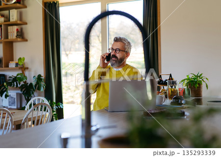 Man working from home while on phone call. Man working from home while on phone call. 135293339