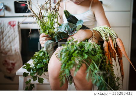 Little girl holding freshly harvested vegetables in home garden. 135293433