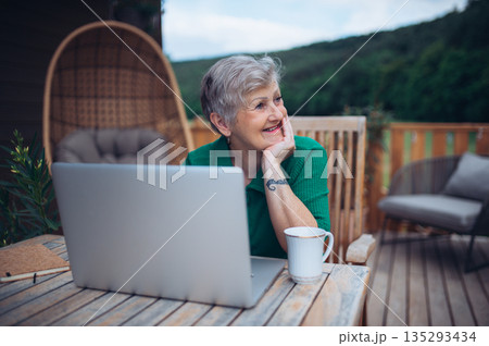 Mature woman sitting on balcony with laptop, working remotely. Mature woman sitting on balcony with laptop, working remotely. 135293434